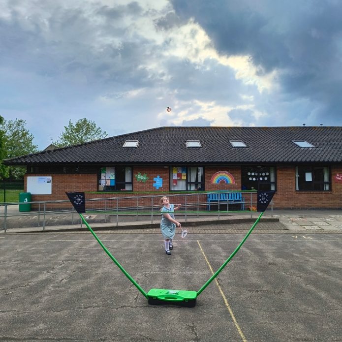 Child playing Badminton using a Sure Shot Quick Fit Set and rackets on a primary school sports court playground