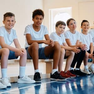 Students sitting on a balance bench in a school sports hall