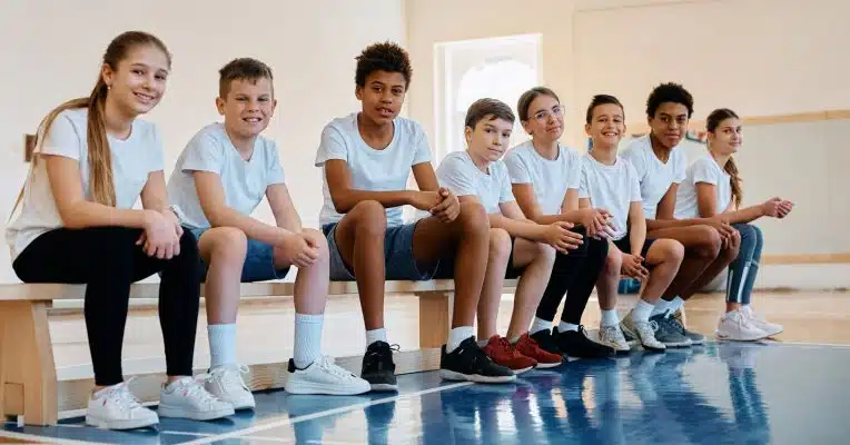 Students sitting on a balance bench in a school sports hall